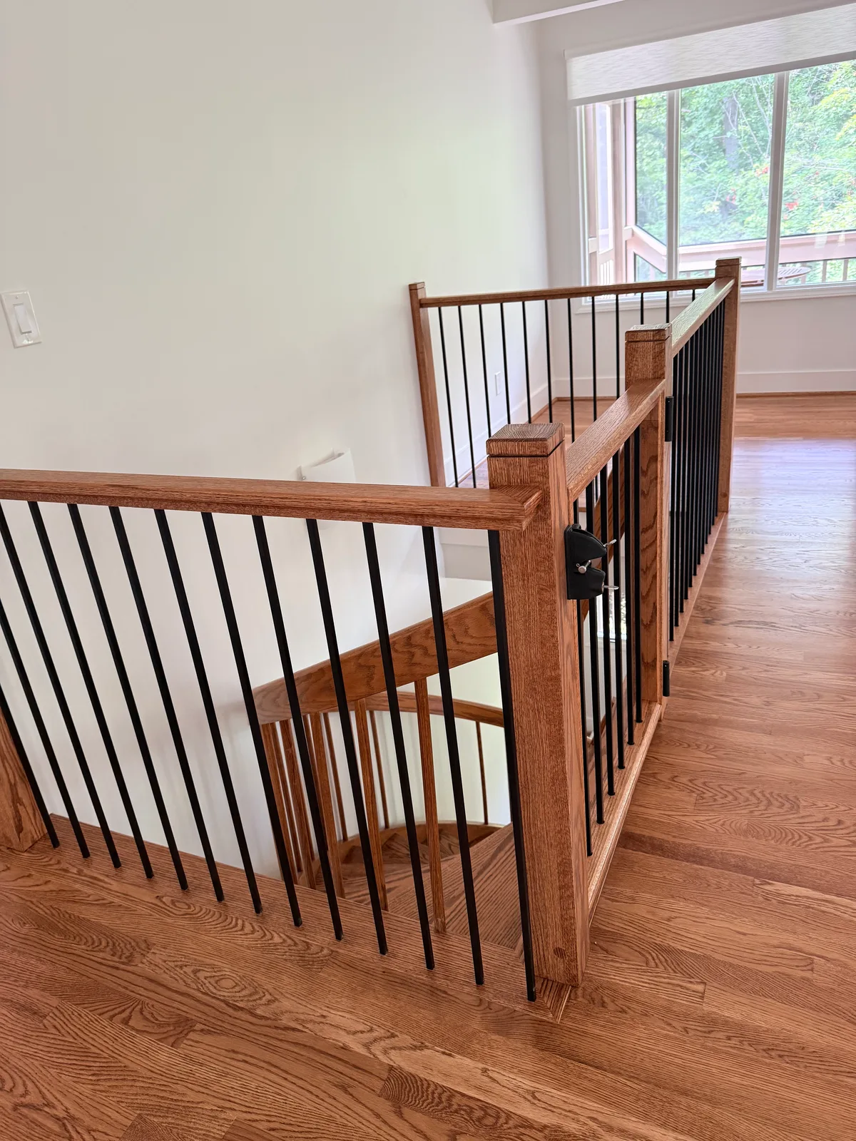 Interior wood stair railing after replacement with black balusters and gate hardware